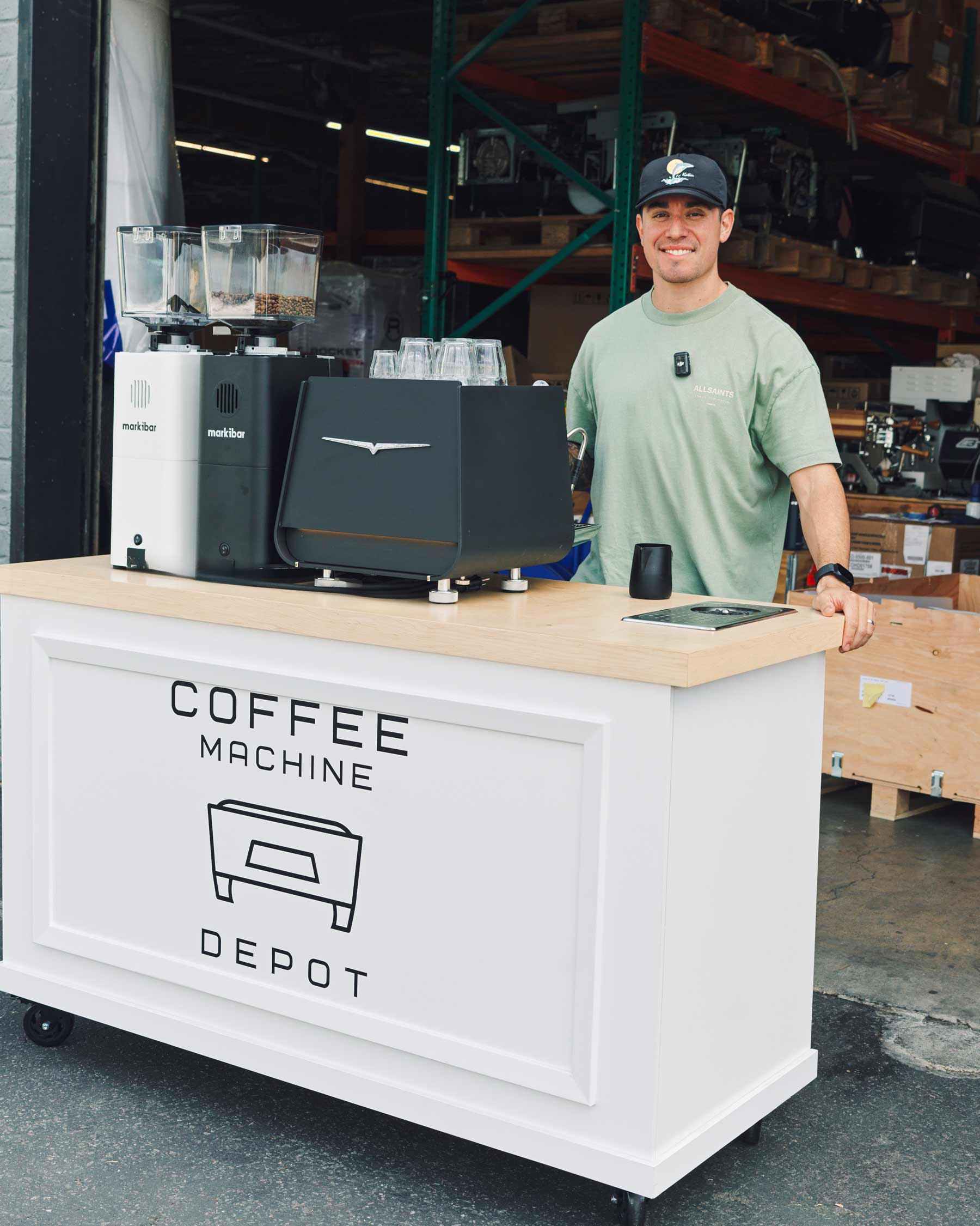 Man standing behind a coffee machine cart with 'Coffee Machine Depot' branding in a warehouse setting.