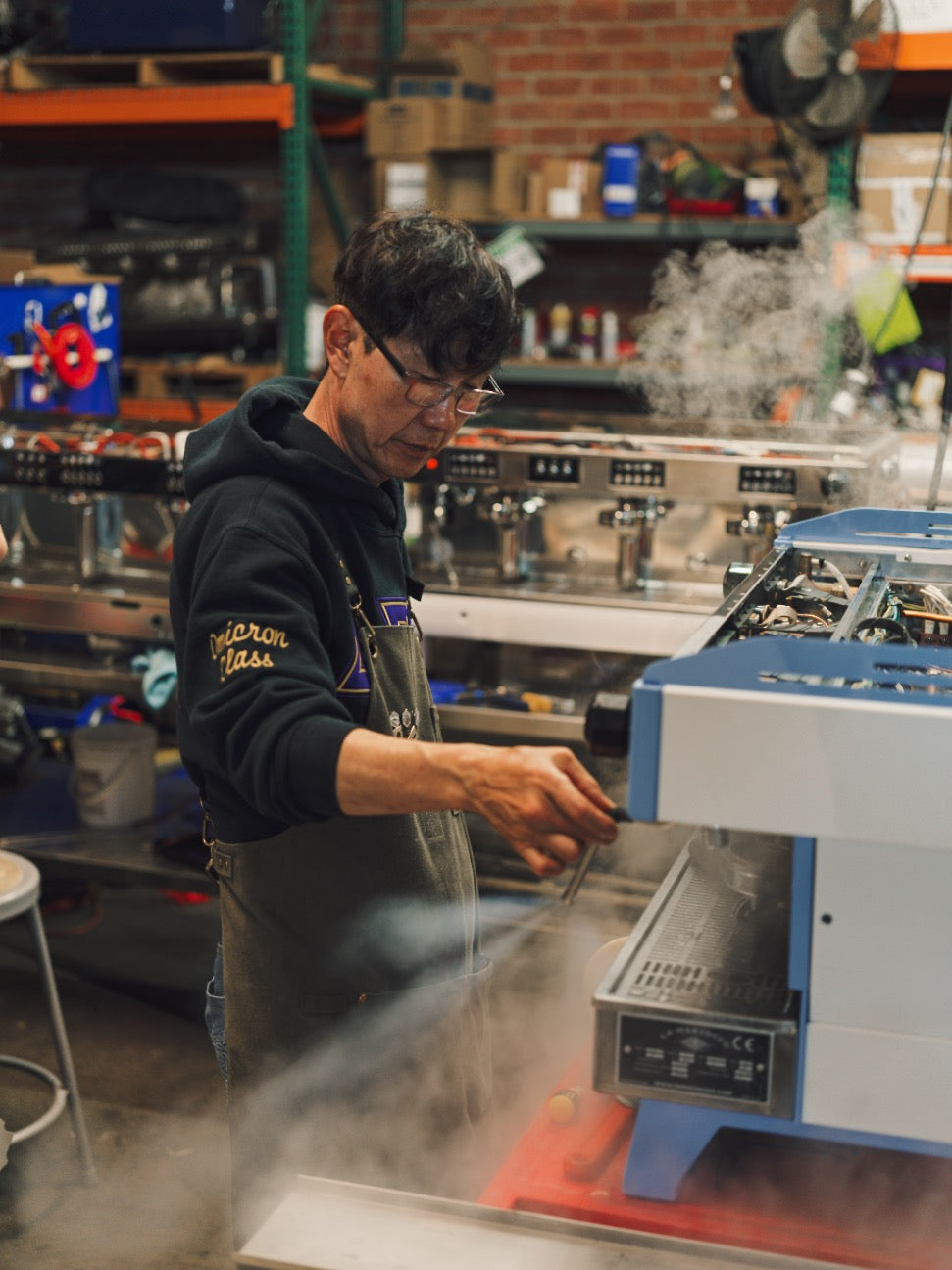 Espresso machine technician performing commercial coffee equipment maintenance and steam wand testing in a professional service workshop.
