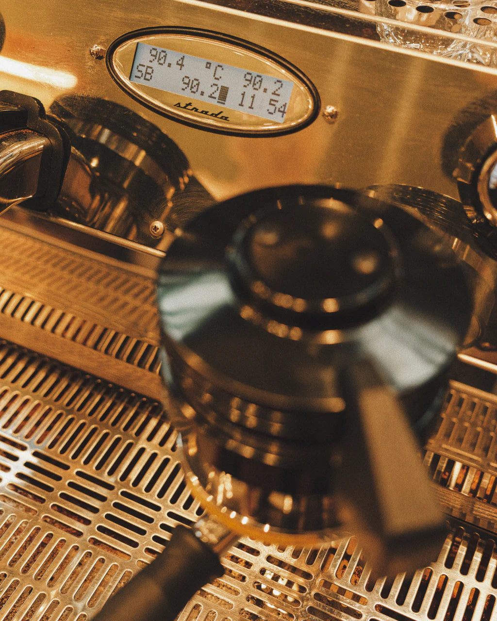 Close-up of a La Marzocco Strada espresso machine showing temperature readings on its digital display and a portafilter resting on the drip tray.