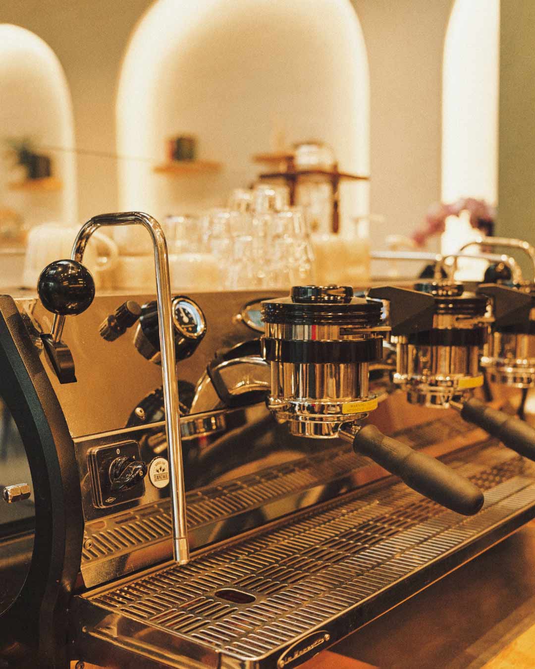 Close-up of a high-end commercial espresso machine with multiple group heads and steam wand in a modern café, set against a warm, minimalist interior