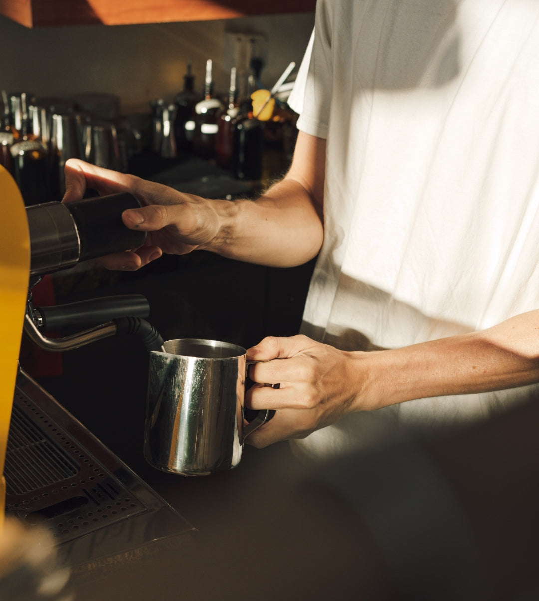 Person making a coffee using a barista machine with a metal cup.