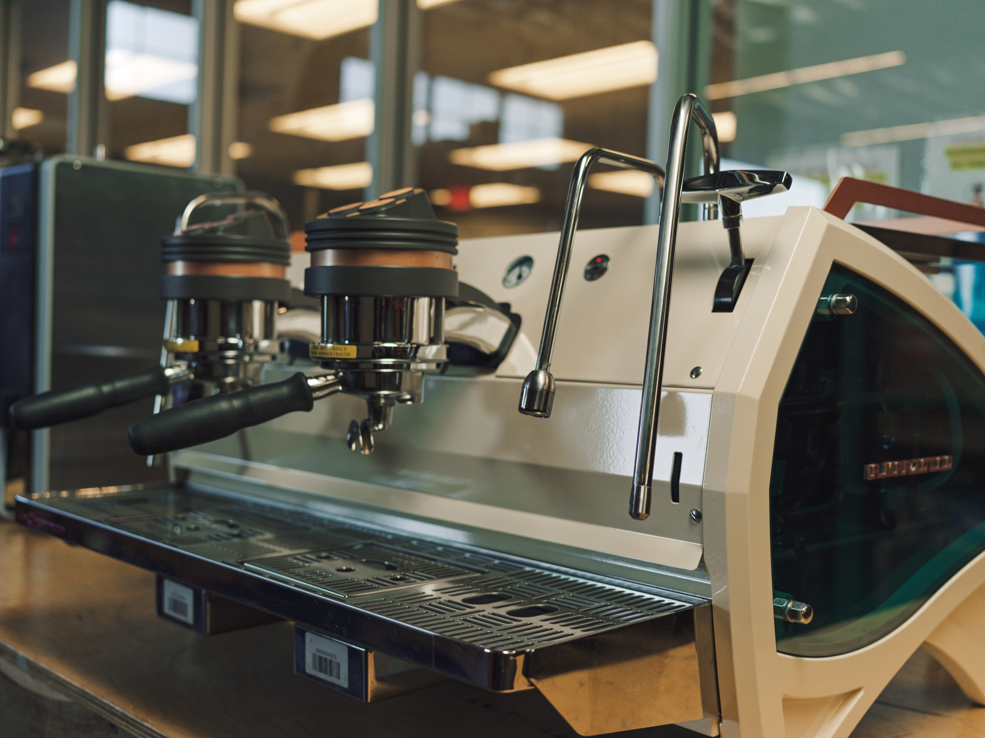 Close-up of a white commercial Rancilio espresso machine with dual group heads and steam wands, set up in a modern coffee shop or training space.